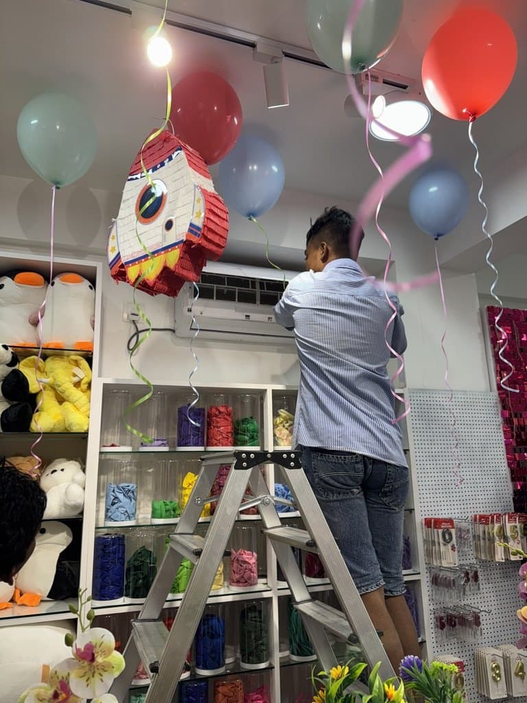 Rishthaa technician on a ladder servicing a wall-mounted split AC in a shop