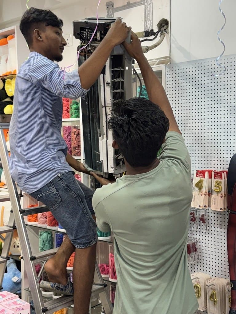 Two Rishthaa technicians servicing an opened split AC indoor unit together